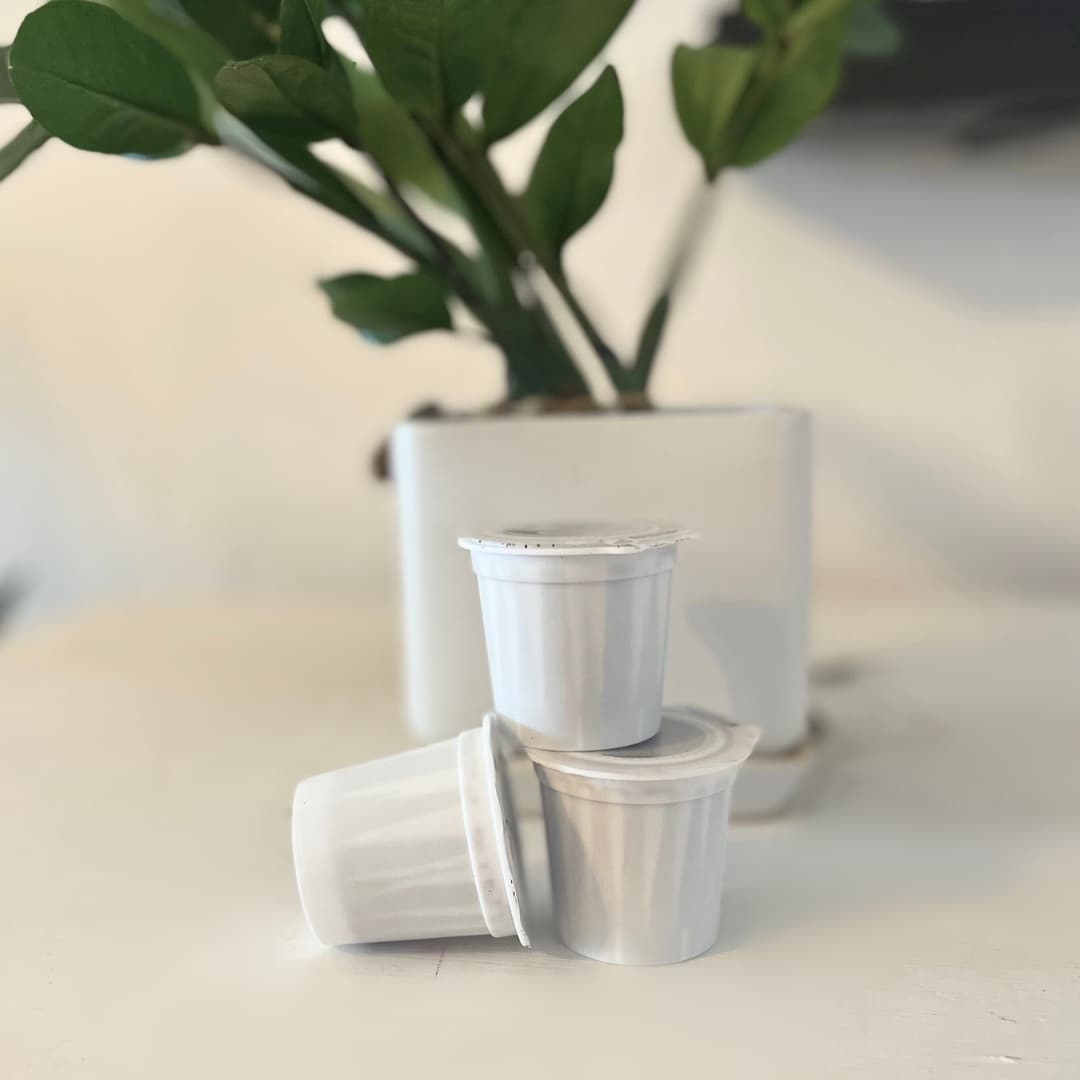 Three Tranquil Coffee Roasters single-serve K-Cups on a cream table with a plant behind